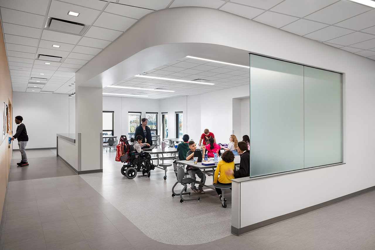 Students gather in small cafeteria separated from corridor by translucent window