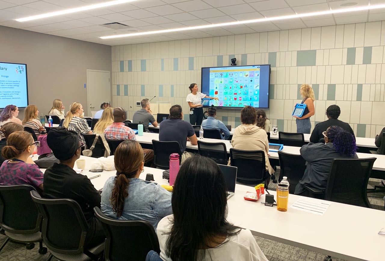 Educational staff receiving training in large conference room with monitors