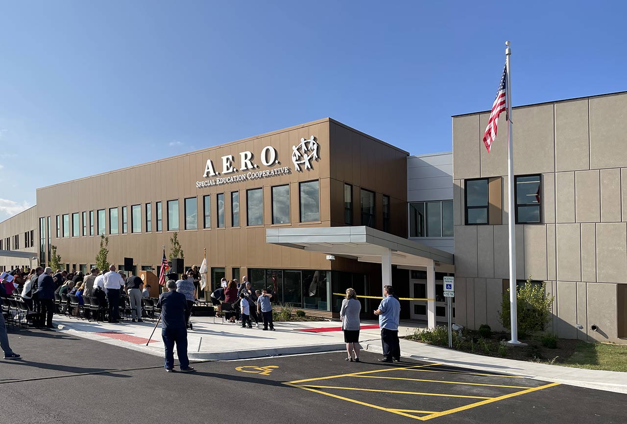 People gathered at school entrance with metal and precast concrete facades and metal canopy.