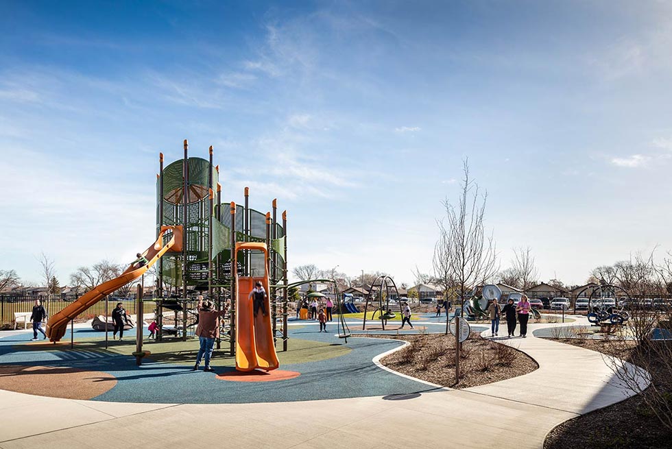 Students and adults on playground with specialized equipment and colorful flooring.