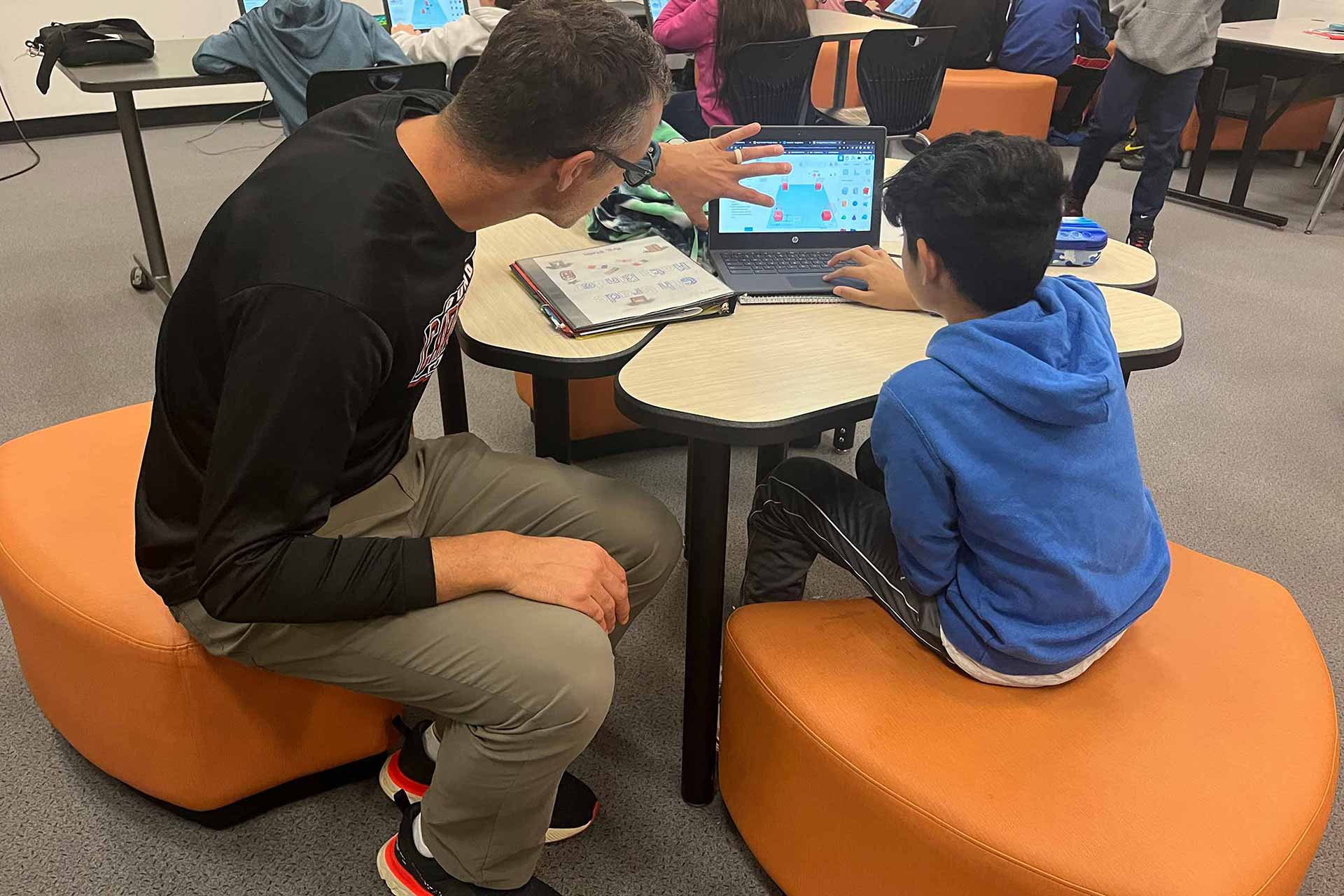 Teacher and student sitting on ottomans and working on computer program