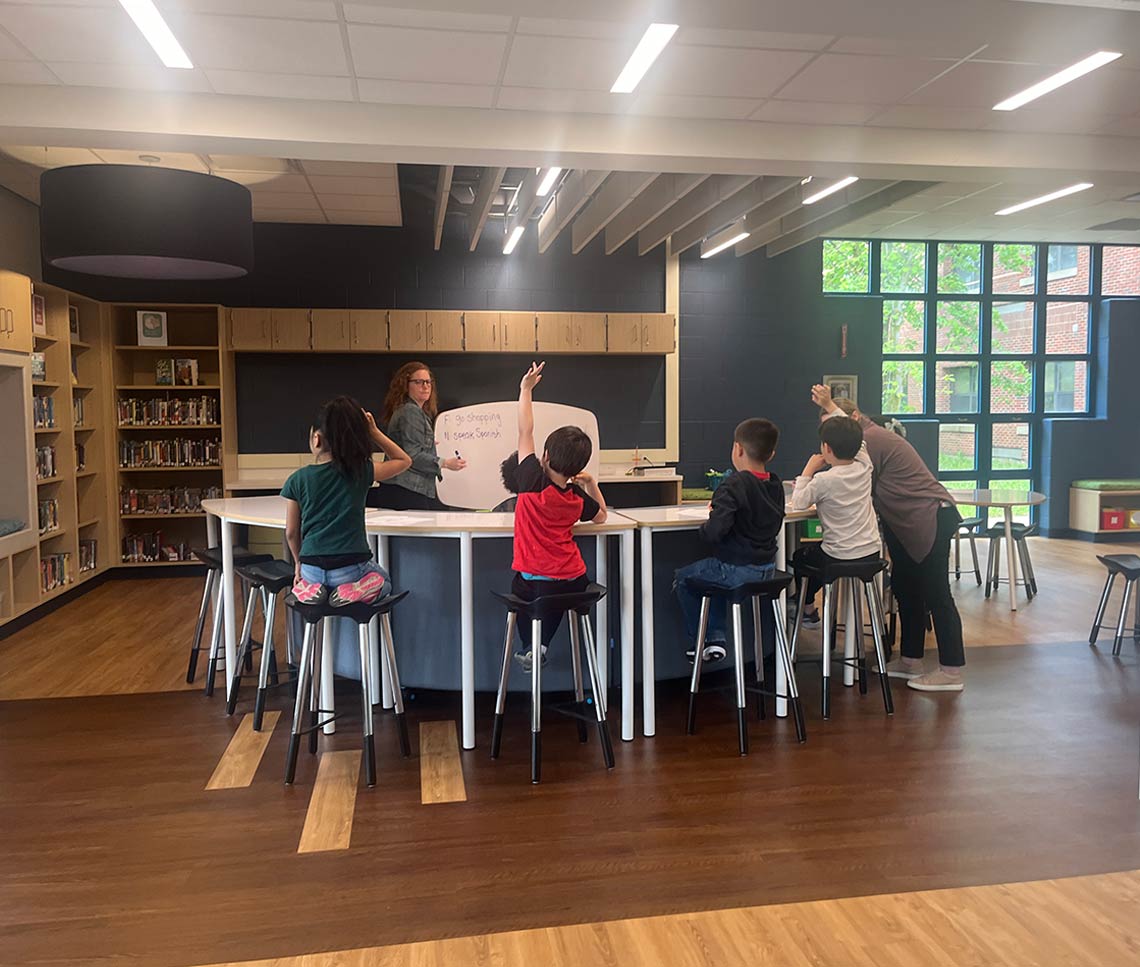 Students in a library doing projects at a table, with views to outdoors