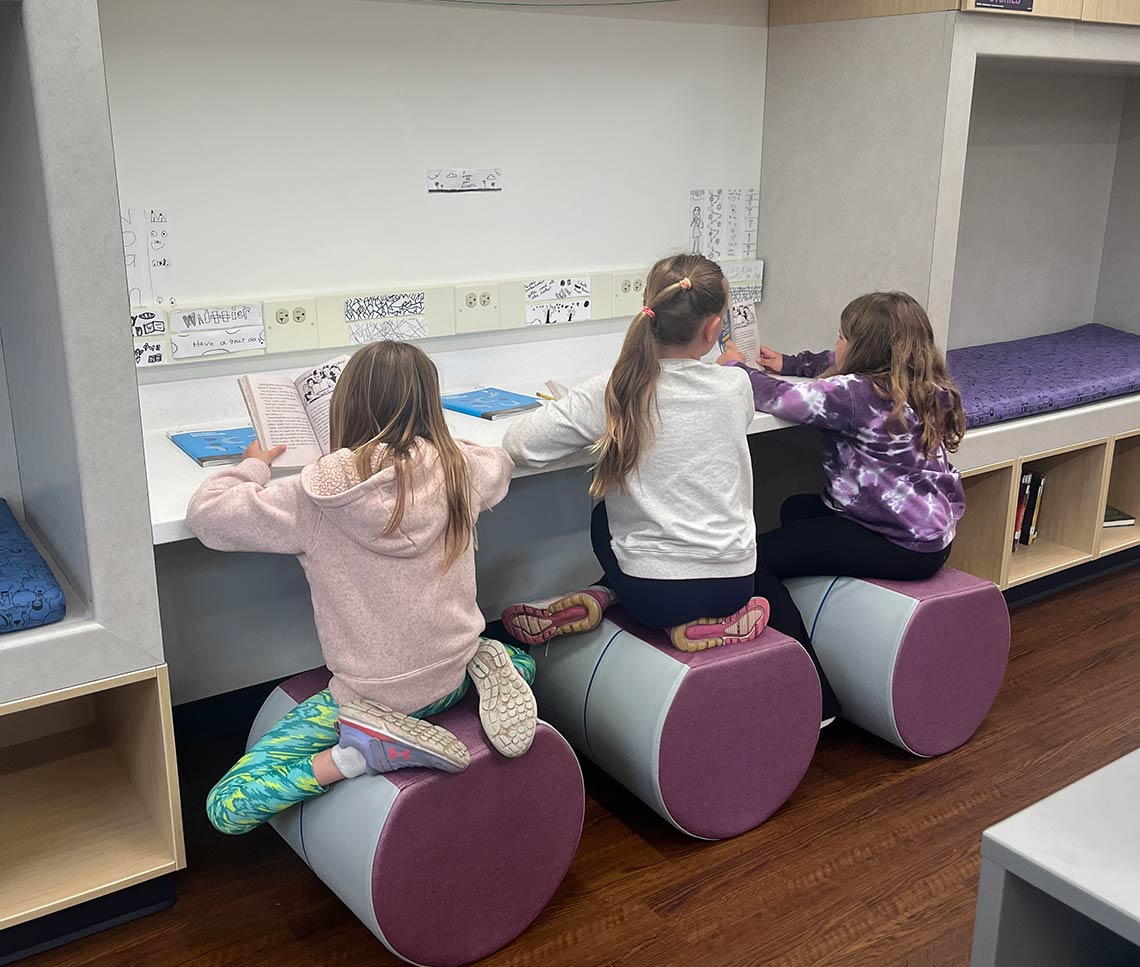 Students sitting on modern furnishings and reading at a library counter