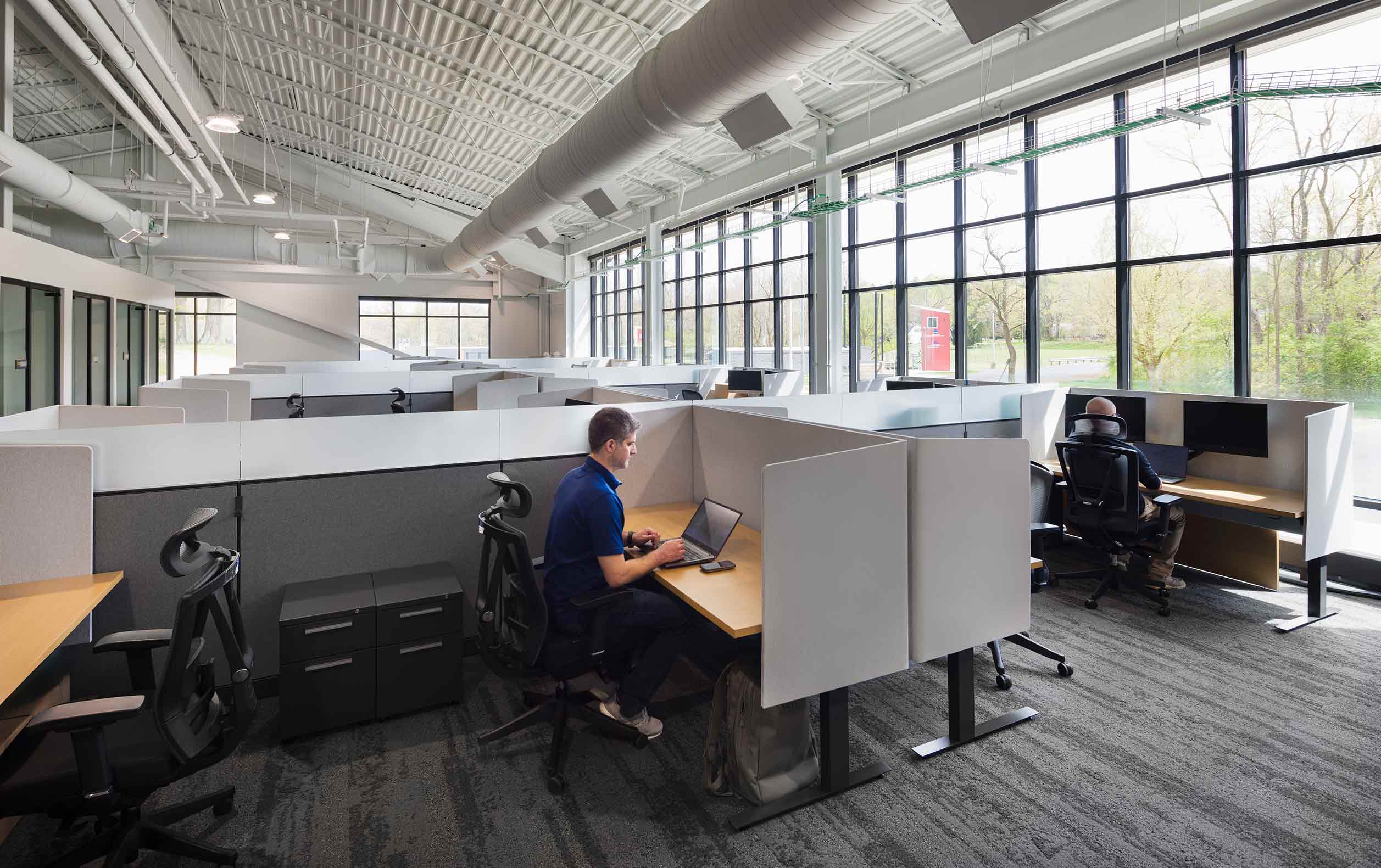 Office bullpen with large glass wall displaying forest
