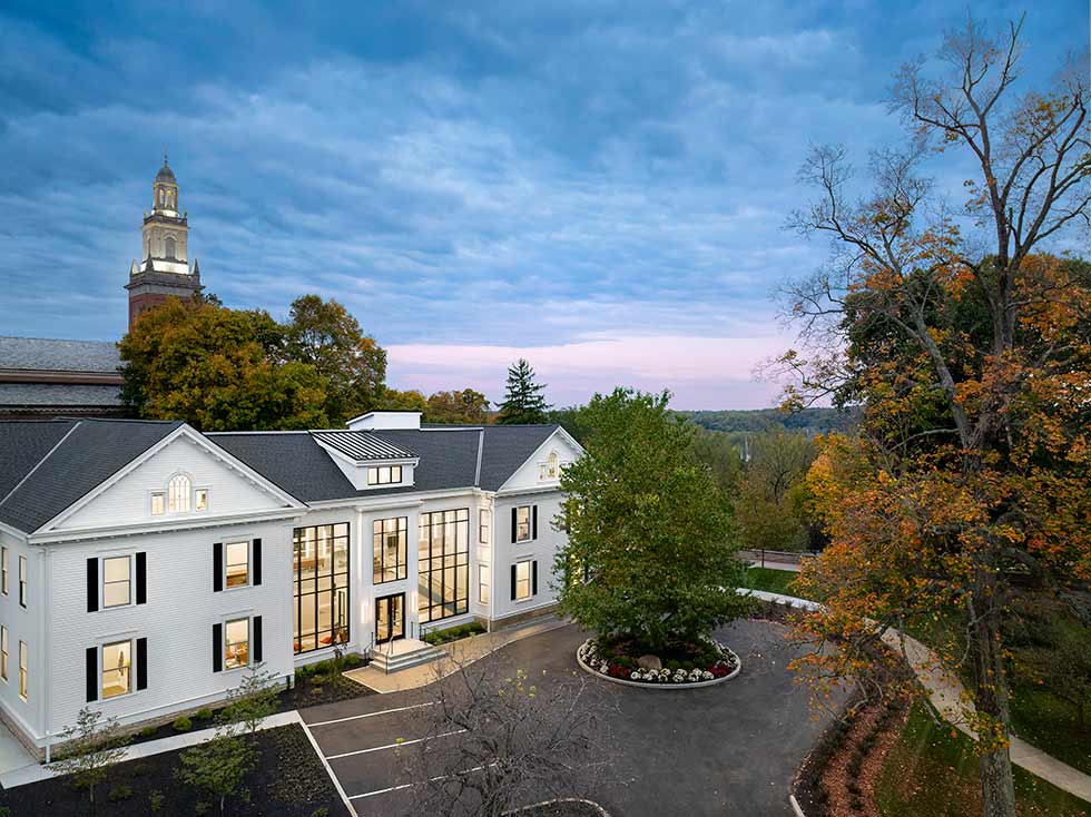 Dusk photo of classical college building with steeple in background.