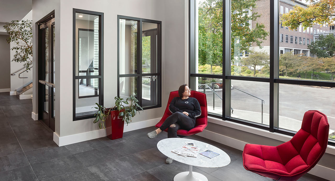 Woman sitting in modern red chair in lobby with window displaying college campus