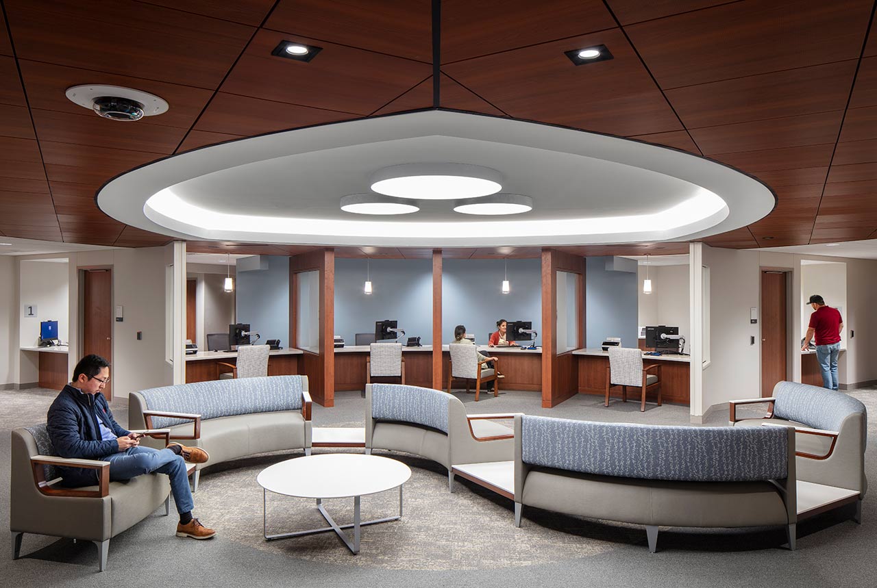 Contemporary healthcare waiting room with check-in areas, curving seats, and wood ceiling